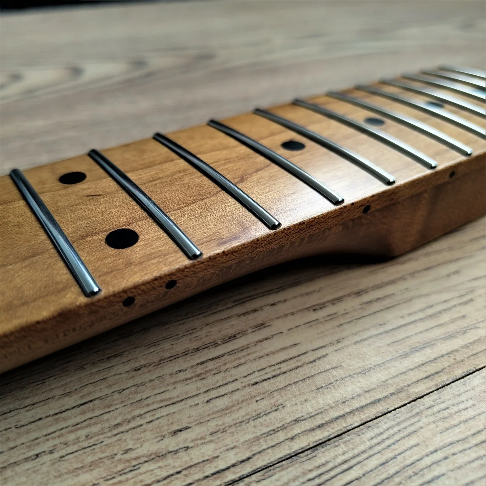 Close-up of polished stainless steel frets on a roasted maple fretboard