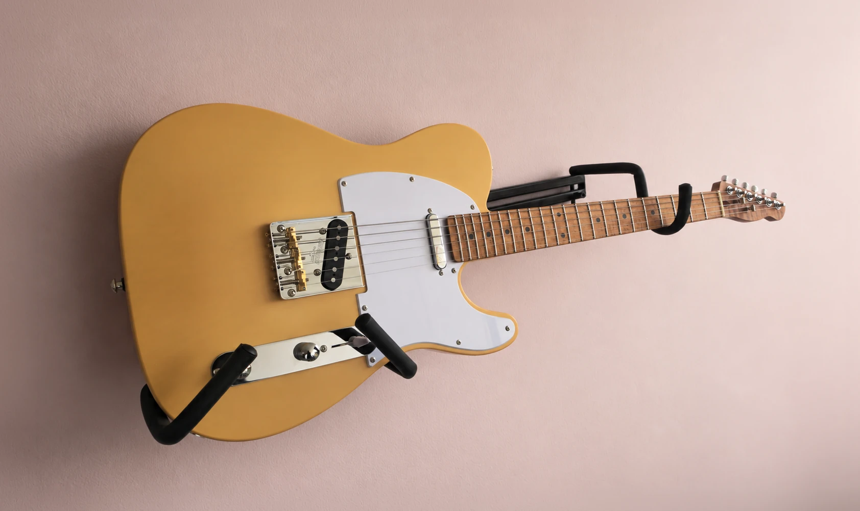 Completed butterscotch T-style guitar mounted against a pale workshop wall