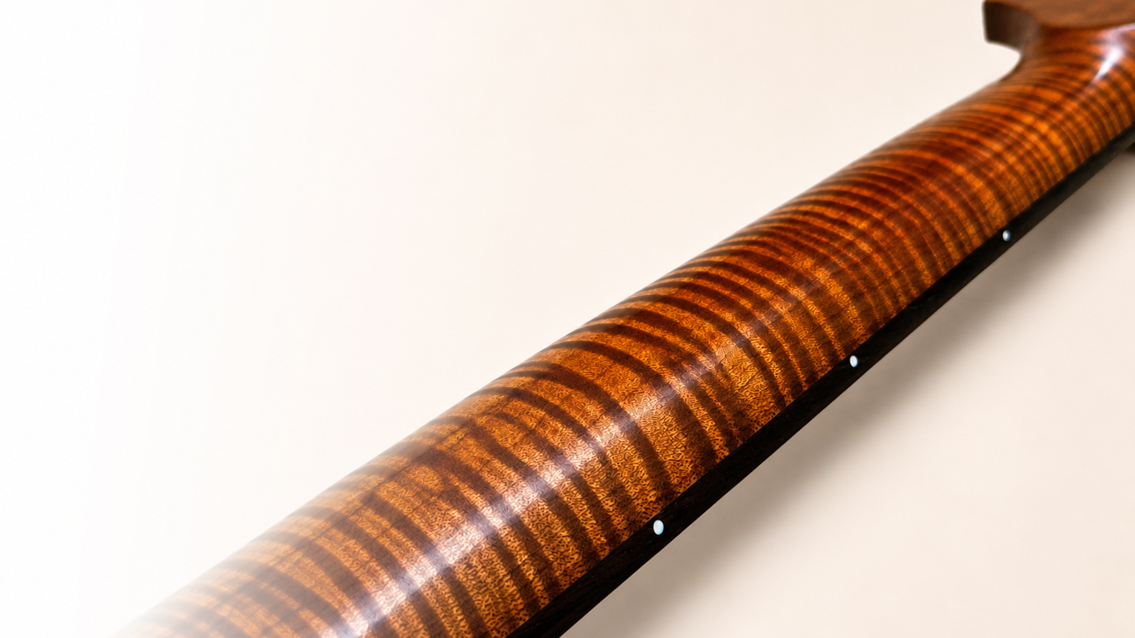Roasted flame maple guitar neck close-up showing figured wood grain and side dots